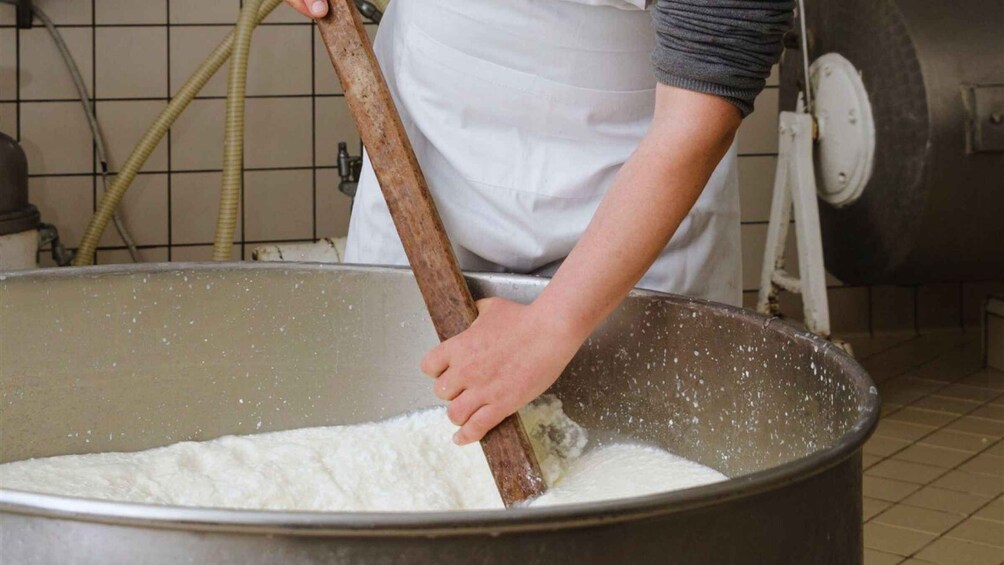 Henkilö sekoittaa suurta kattilaa, jossa on valkoista ainetta, todennäköisesti taikinaa tai seosta, keittiössä. 1