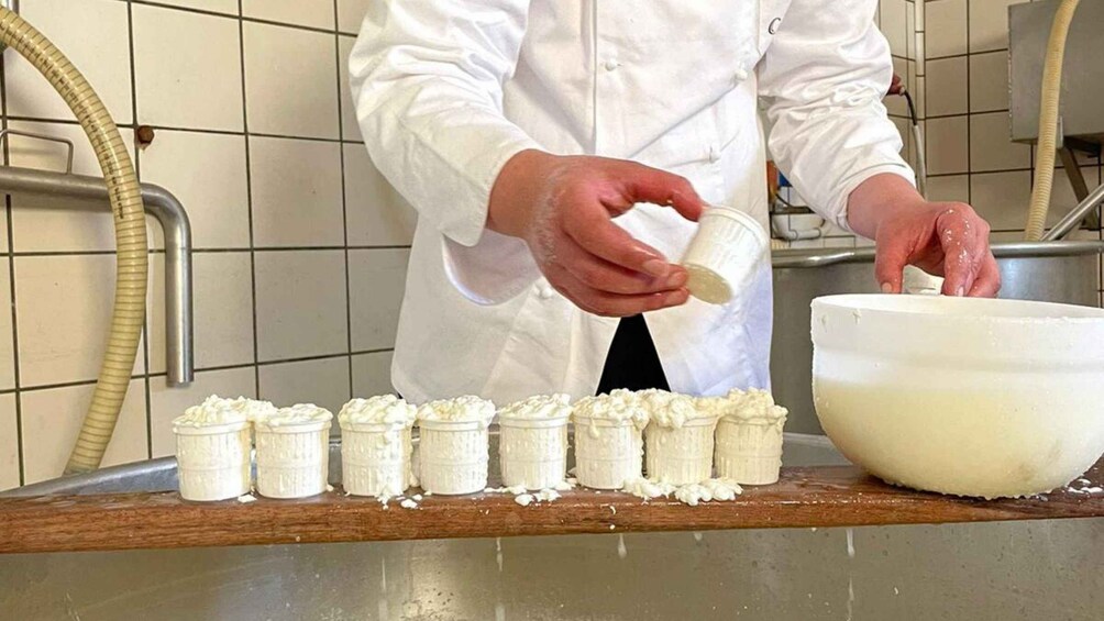 Henkilö, jolla on valkoinen kokkitakki, kaataa taikinaa muffinivuoihin keittiön työtasolla. 3