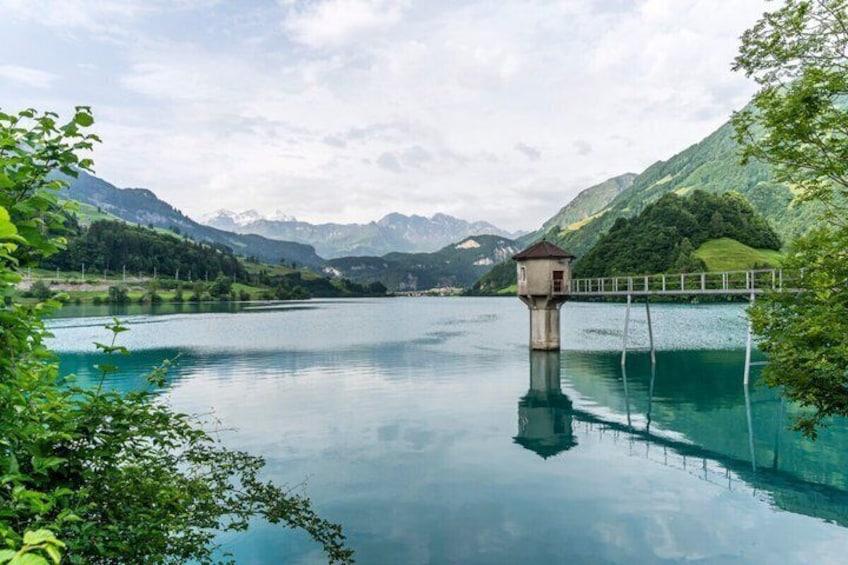 Un lago tranquilo con una torre pequeña y un puente, rodeado de colinas y montañas verdes y exuberantes. 3