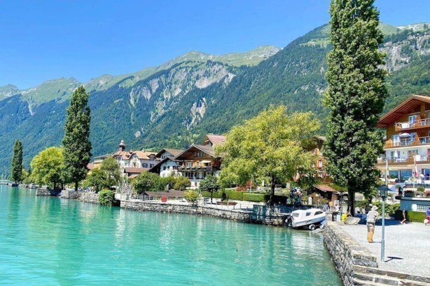 Un pueblo a orillas de un lago, con edificios, árboles y montañas al fondo. 5
