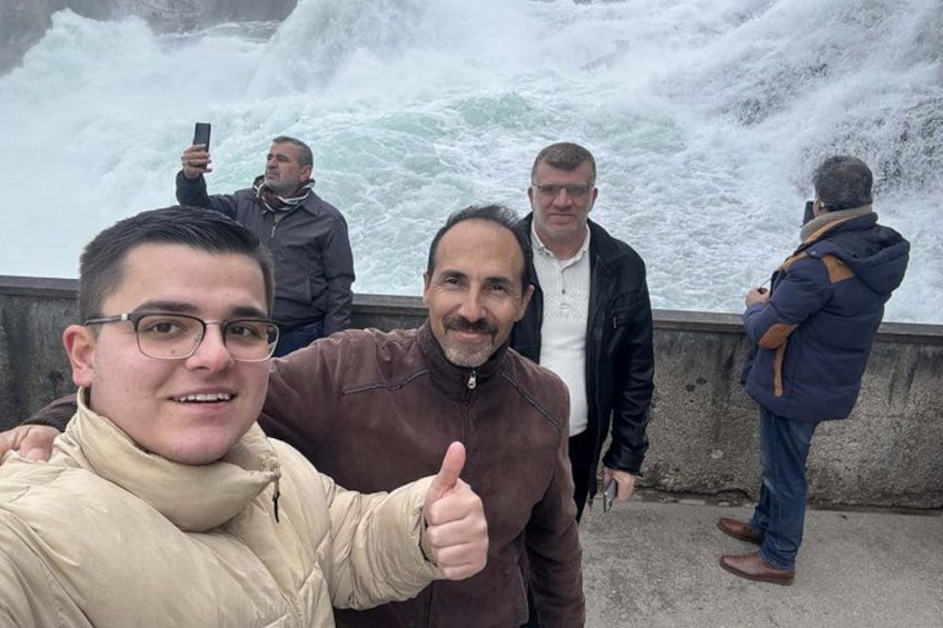 A group of people standing by a rocky waterfront with waves crashing against the shore. 2