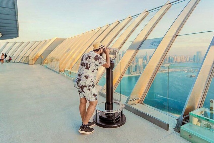 Une personne prend une photo avec un appareil photo sur une plateforme d’observation en verre, avec une vue sur la ville en arrière-plan. 4