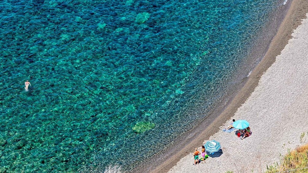 A beach with clear turquoise water, people swimming, and others relaxing under umbrellas. 2