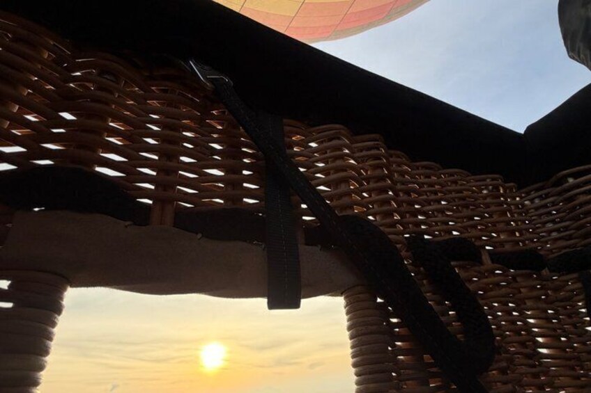 A wicker structure with a woven pattern, a metal support, and a sunset in the background. 2
