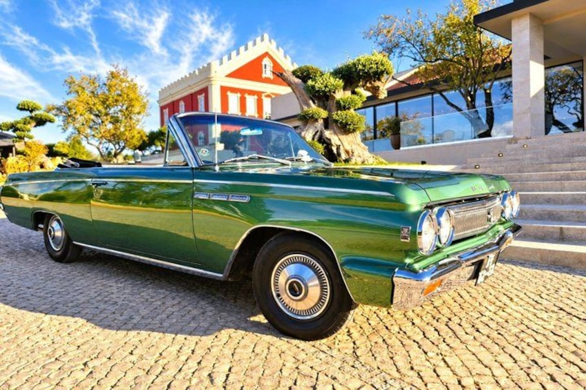 A green vintage car parked on cobblestone. 1