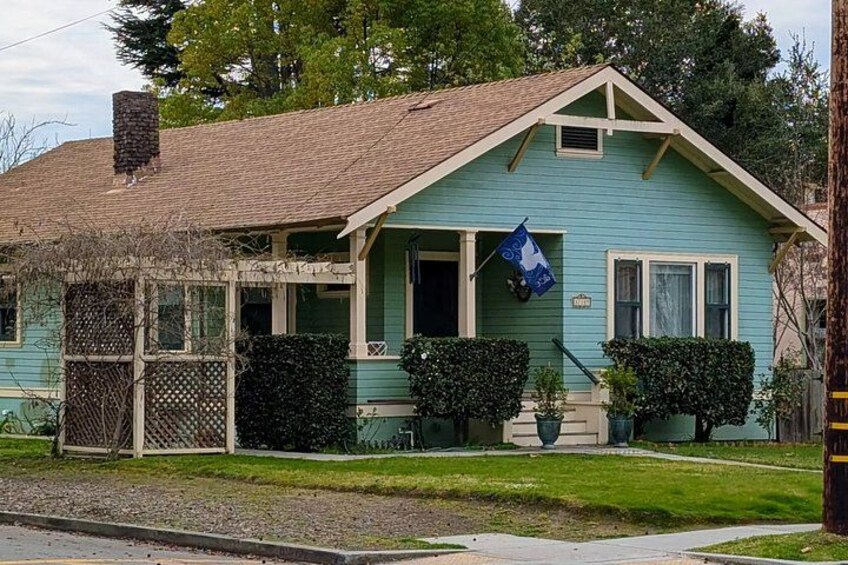 A light blue house with a brown roof, a porch, and a blue flag. 4