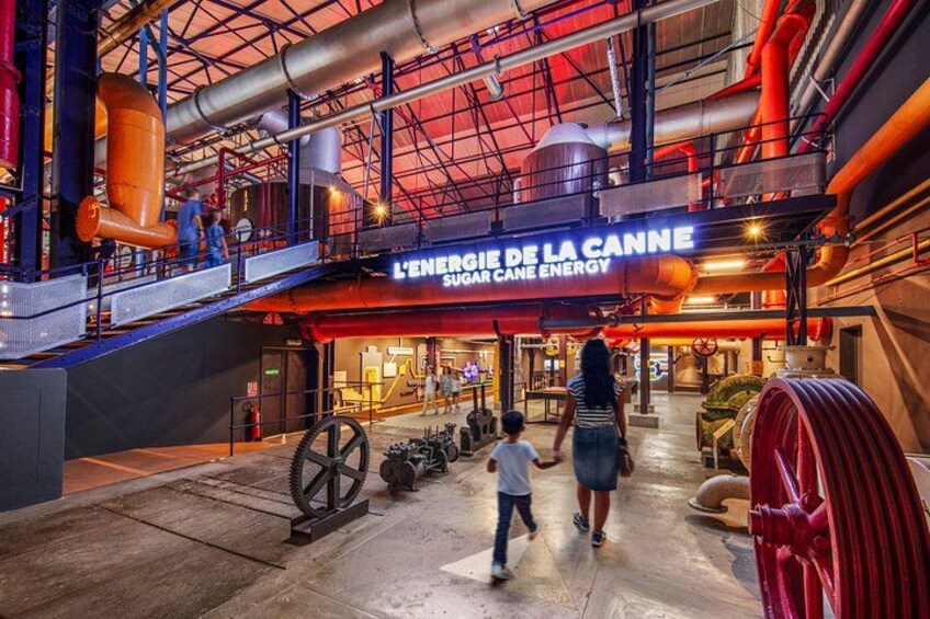 Un espacio interior industrial con un letrero que dice 'L'ENERGIE DE LA CANNE' y grandes tuberías y ruedas. 2