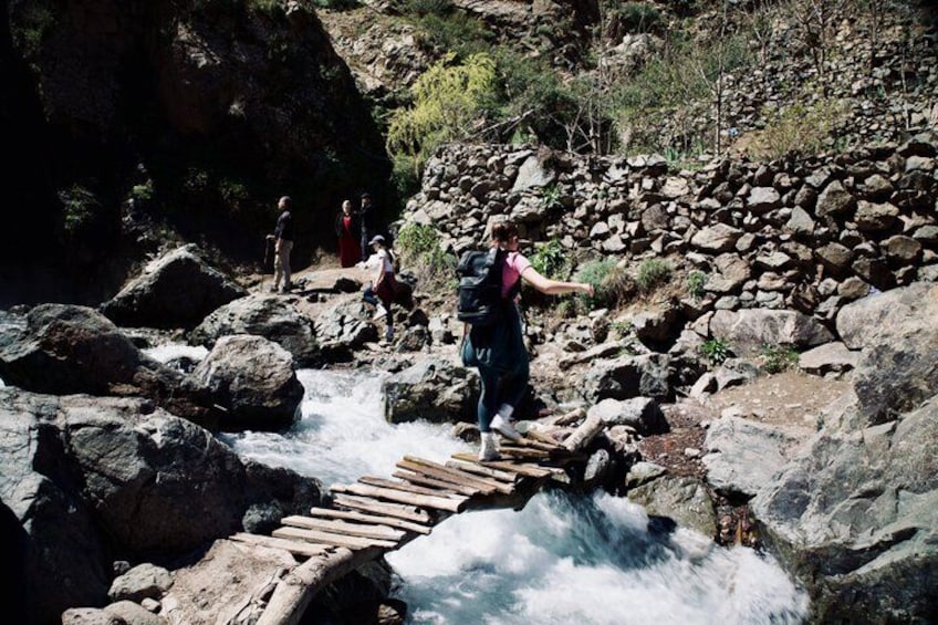 A wooden bridge over a flowing river with hikers on the surrounding rocky terrain. 4