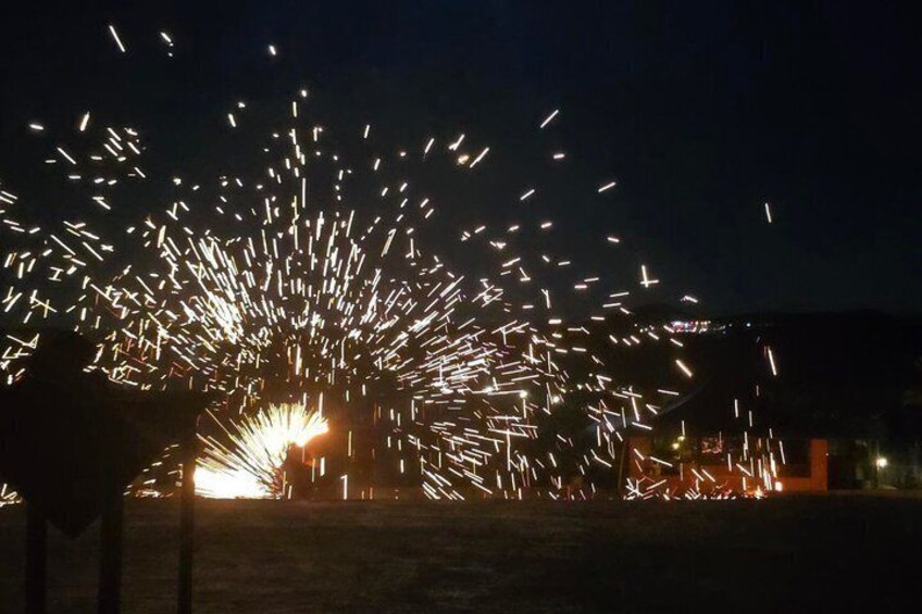 Scintille che si alzano da una fonte a terra, forse fuochi d'artificio, in un ambiente esterno buio. 5