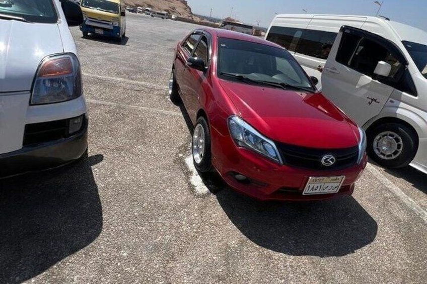 A red car parked in a lot with other vehicles, including a white van and a yellow car. 5