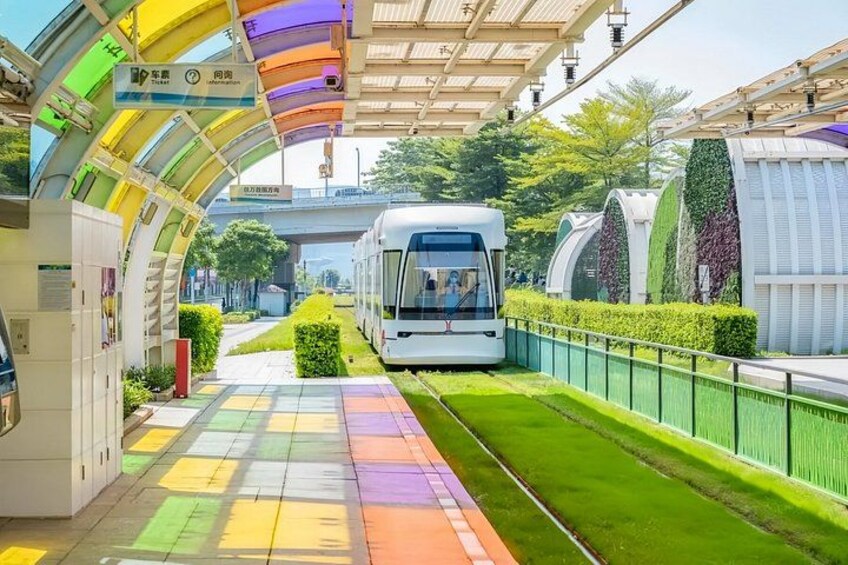 A modern bus station with a colorful roof, a white bus, and green landscaping. 1
