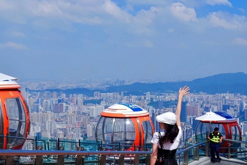 A cityscape with a person raising their hand, a glass-enclosed observation pod, and a distant mountain range. 4