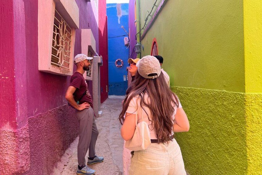 A narrow alley with colorful buildings, a blue door, and a person wearing a cap. 3