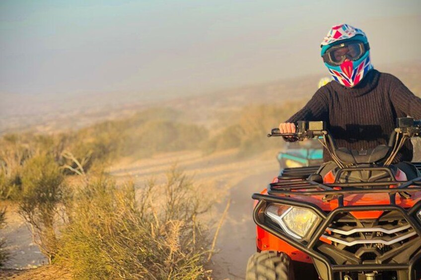 A person riding an ATV on a dirt trail with sparse vegetation. 2
