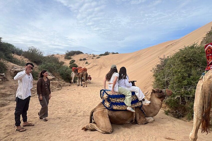 A desert landscape with people riding camels. 2