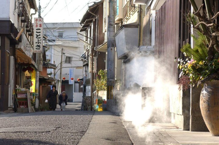 A narrow street with buildings, a large potted plant, and smoke rising from a source on the right. 5