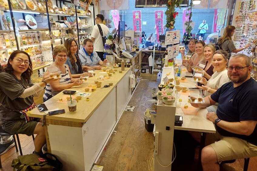 En gruppe mennesker sidder ved et langt bord på en café, med forskellige retter og drikkevarer på bordet. 4