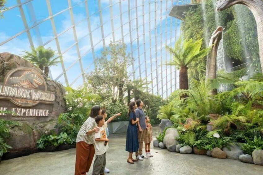 Et område med tema fra Jurassic World, med en stor dinosaur-statue, frodigt grønt og en konstruktion med glastag. 5