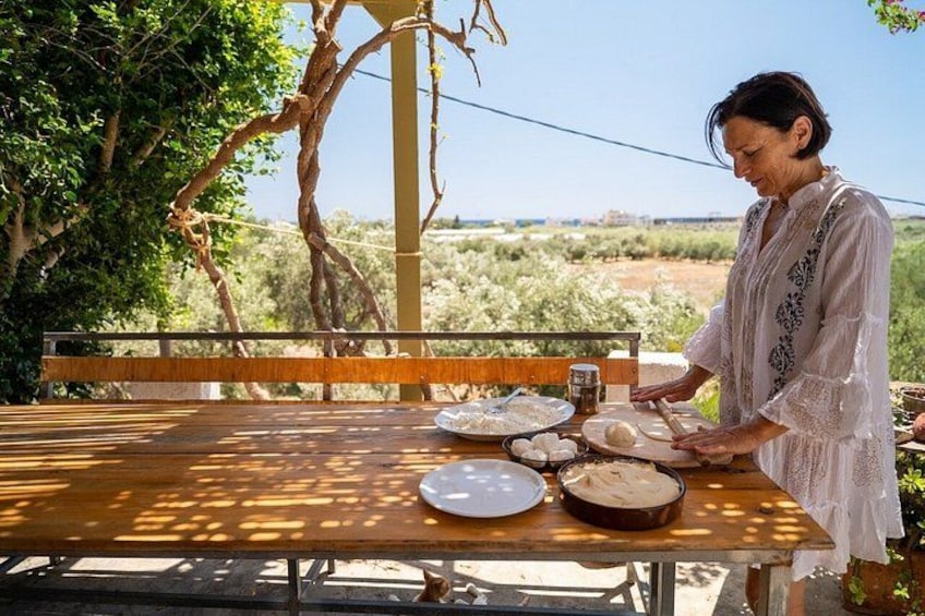 A person preparing food outdoors with a table, a bench, and a view of a natural landscape. 1