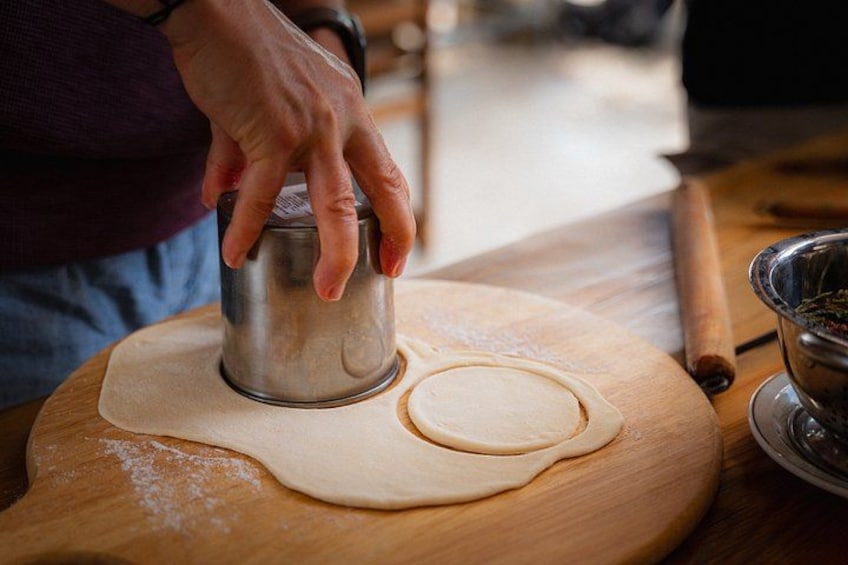 A person using a metal cutter on dough on a wooden board. 3