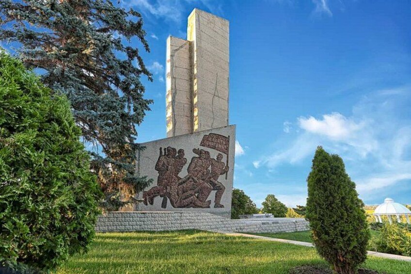 Ett monument med en reliefskulptur, omgivet av grönska och en klar himmel. 2