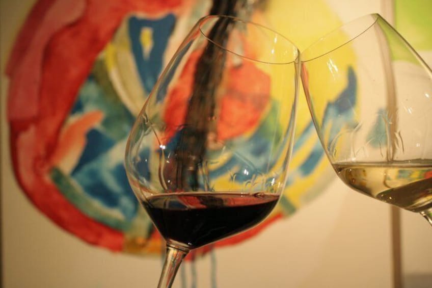 Dos copas de vino, una con vino tinto y otra con vino blanco, frente a un cuadro abstracto de colores. 4