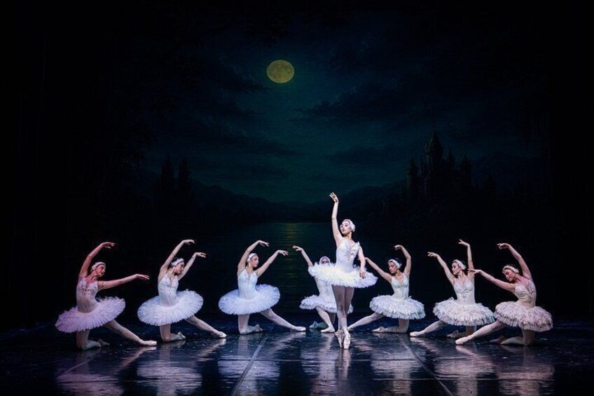 A ballet performance with dancers in white tutus on a stage with a dark background and a full moon. 4