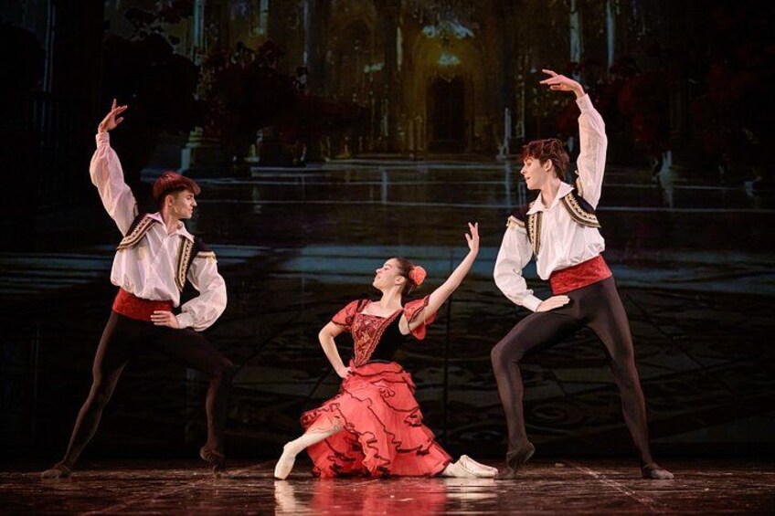 A ballet performance with dancers in period costumes on a stage with a dark background and architectural elements. 4
