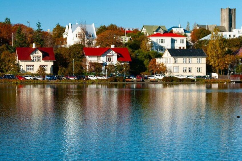 A lake with buildings reflecting on the water, surrounded by trees and a clear sky. 2