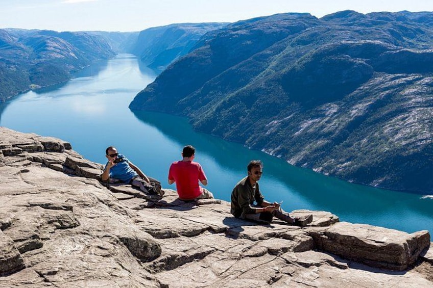 Trois personnes sont assises sur un promontoire rocheux, d’où elles dominent un lac d’un bleu profond, entouré de montagnes. 3