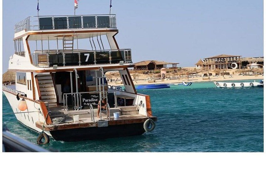 A boat with the number 7, named Paradise, docked at a beach with other boats and a building in the background. 2