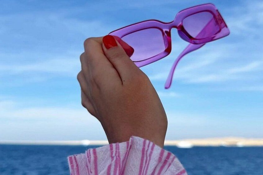 A hand holding pink sunglasses with a clear sky and ocean in the background. 5