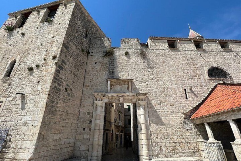 A historic stone building with a prominent entrance, a tower, and a red-tiled roof. 2