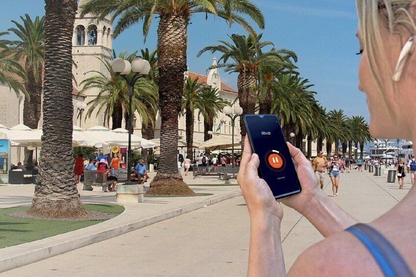 A person holding a smartphone with a red circle icon, palm trees, and a building with a clock tower in the background. 5