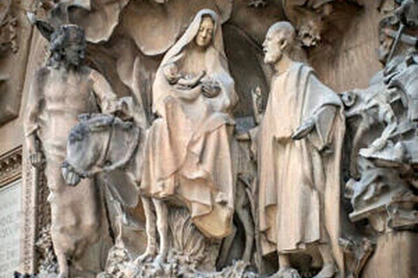 Escultura de piedra de una mujer sosteniendo a un niño, flanqueada por dos figuras, sobre un fondo rocoso. 2