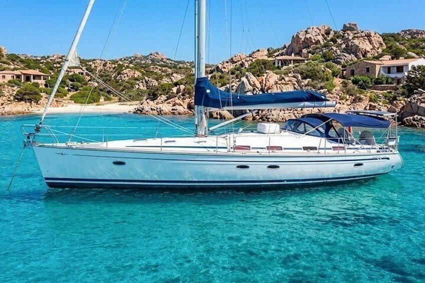 Un velero en aguas turquesas cristalinas con colinas rocosas y casas al fondo. 1