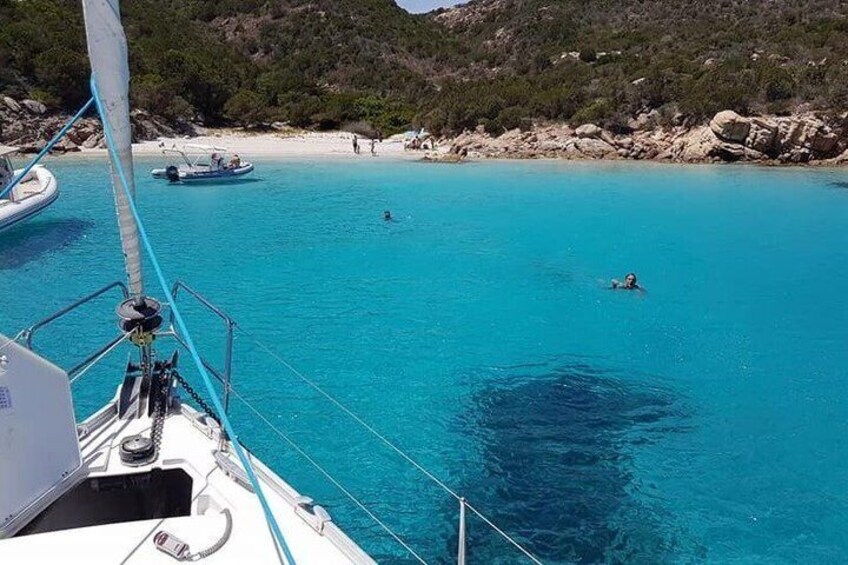 A sailboat on turquoise water with a beach and rocky landscape in the background. 4