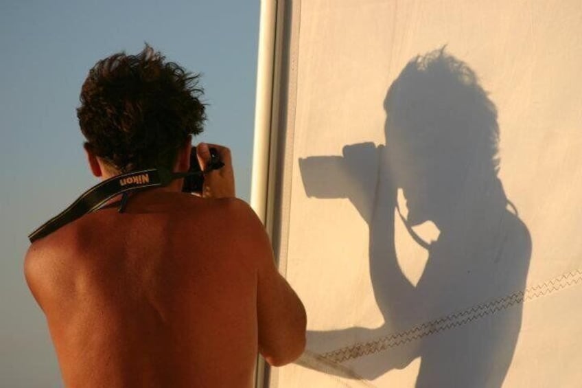 A person taking a photograph with a camera, wearing a Nikon strap. 5