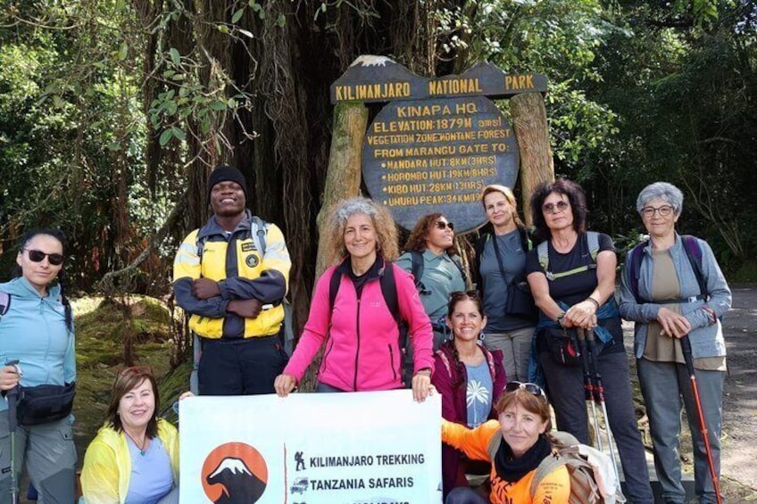 Eine Gruppe von Menschen im Kilimanjaro-Nationalpark, mit einem Schild, das eine Höhe von 1879 m angibt. 3