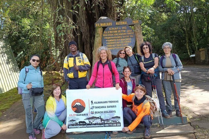 Eine Gruppe von Menschen posiert vor einem Schild im Kilimanjaro-Nationalpark. 1