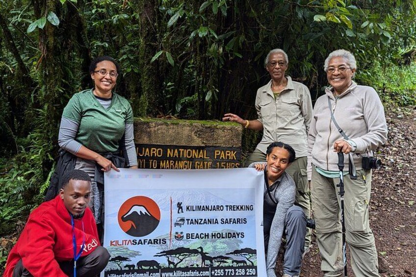A group of people standing in front of a sign for Kilimanjaro Trekking and Tanzanian safaris. 3