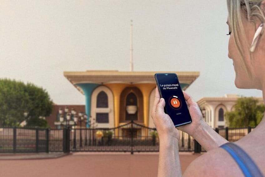 Una persona sosteniendo un teléfono inteligente con una aplicación de música abierta, de pie frente a un edificio colorido con ventanas arqueadas y una cerca. 5