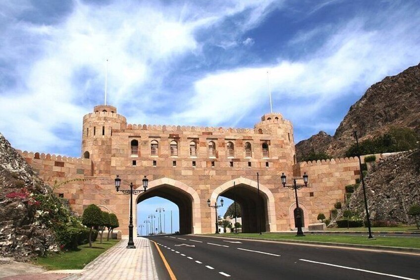 Un gran arco de piedra con estructuras similares a castillos a ambos lados, que da paso a una carretera. 2