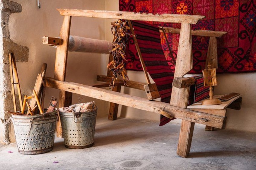 Un métier à tisser traditionnel, doté d’un cadre en bois, d’un tissu rouge à motifs et de deux seaux en métal contenant des outils. 3