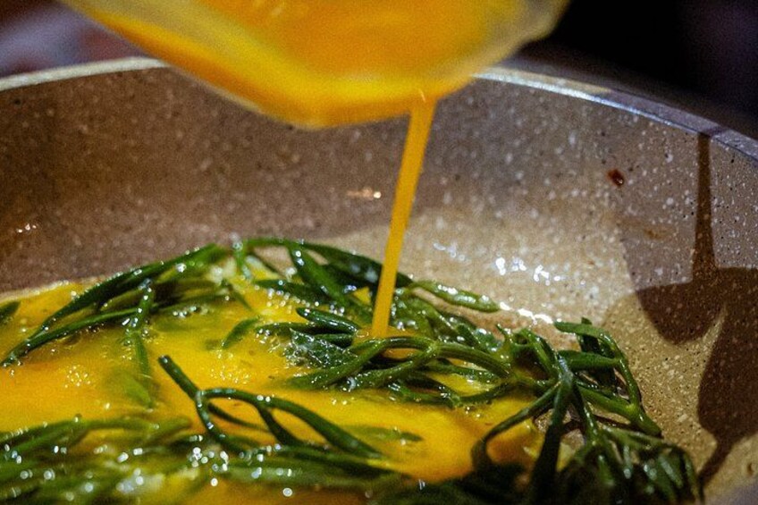 A pan with eggs and green herbs being cooked. 2