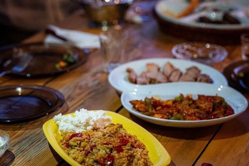 A wooden table with various dishes, including a yellow plate with a rice dish, a white plate with sliced meat, and a red dish with vegetables. 3