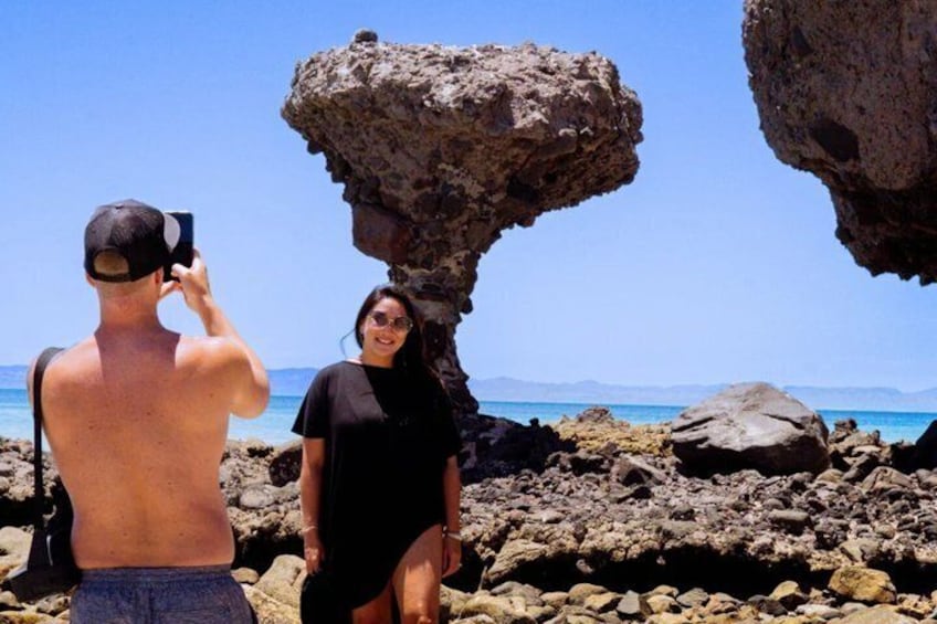Una persona fotografiando a una mujer cerca de una costa rocosa con una formación rocosa destacada. 1