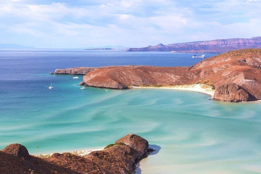 Un paisaje costero con aguas turquesas cristalinas, formaciones rocosas y montañas al fondo. 4