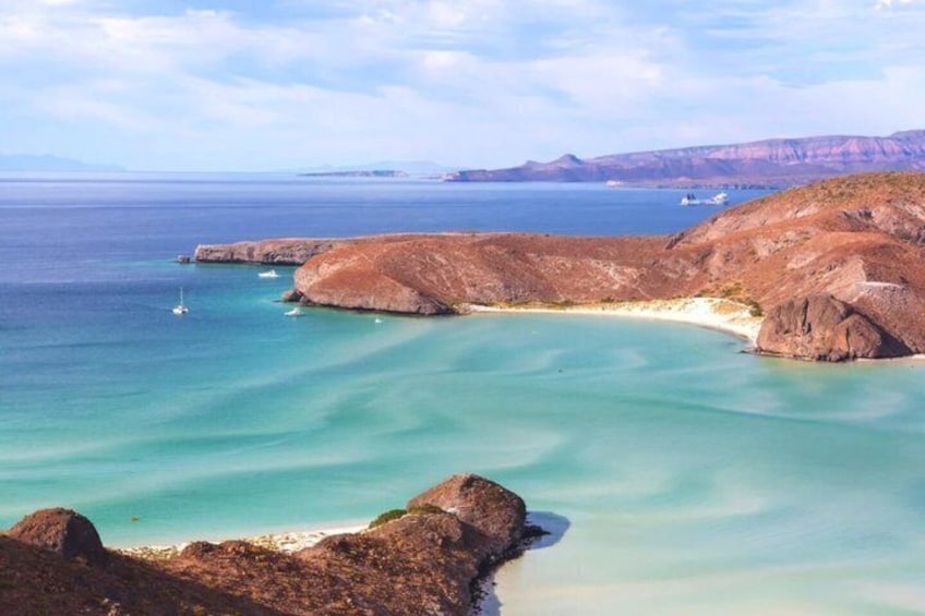Un paisaje costero con aguas turquesas cristalinas, formaciones rocosas y montañas al fondo. 4