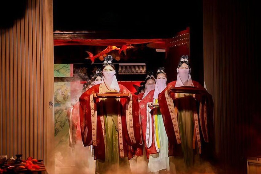 A traditional performance with actors in elaborate costumes and masks, set in a dimly lit indoor space with a red backdrop. 2